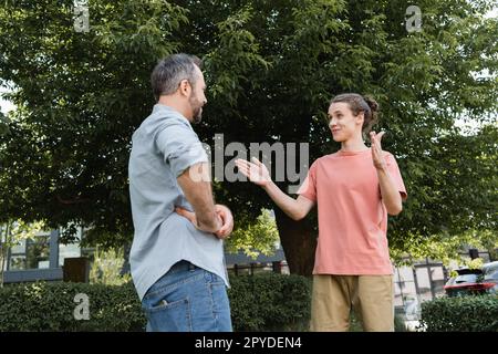 Glücklicher Teenager, der große Geste zeigt, mit Händen in der Nähe des bärtigen Vaters im Park, Stockbild Stockfoto