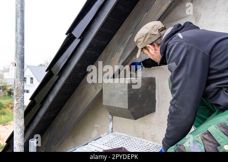 Handwerker, die Holzbeizen auf einen Dachbalken an der Außenseite eines Hauses auftragen Stockfoto