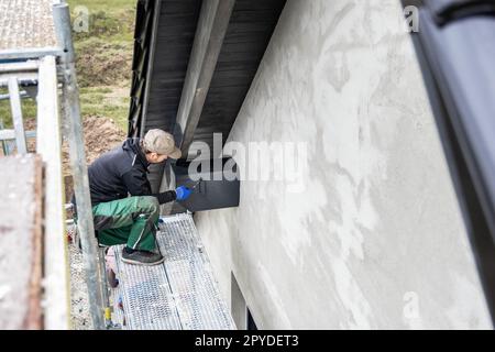 Handwerker, der Holzbeize auf einen Dachbalken eines Hauses mit Giebeldach aufbringt Stockfoto