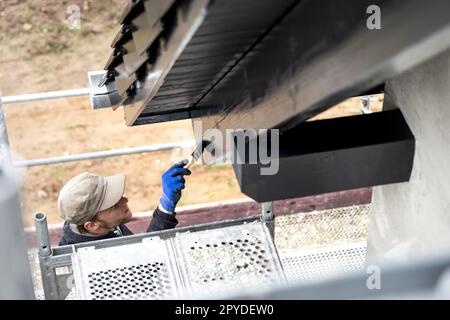 Handwerker, der Farbe auf einen Sparren und einen Dachbalken an der Außenseite eines Hauses aufträgt Stockfoto