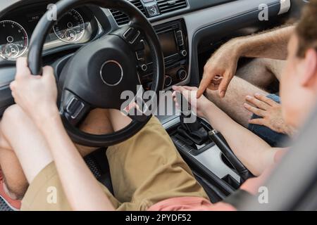 Blick aus dem großen Winkel auf einen Teenager, der das Lenkrad hält und den Gang wechselt, während er mit dem Auto neben seinem Vater fährt, Stockbild Stockfoto