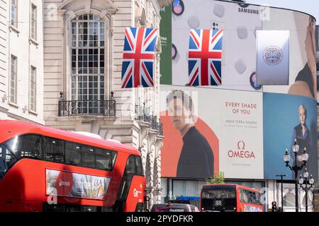 Nur vier Tage vor der Krönung von König Karl III., nach dem Tod seiner Mutter, Königin Elizabeth II. Im letzten Jahr, hängen die Flaggen von Union Jack neben Omega Uhren Werbung, die vom Schauspieler Eddie Redmayne, am Piccadilly Circus, am 3. Mai 2023, in London, England, unterstützt wird. Stockfoto