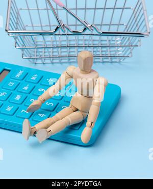 Eine Holzpuppe und ein blauer Taschenrechner, hinter einem Miniatur-Einkaufskorb Stockfoto