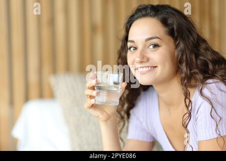 Eine glückliche Frau, die Wasserglas hält, sieht dich an Stockfoto