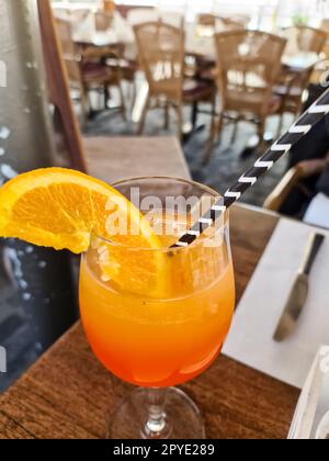 Ein Orangencocktail mit einem Strohhalm und einer Orangenscheibe in einem Glas mit einem sanften Hintergrund eines Restaurants. Stockfoto