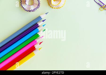 Die Buntstifte in den Ecken sind mit Spänen und farbigen Büroklammern auf hellgelbem Hintergrund für Büro- und Schularbeiten geschärft. Stockfoto