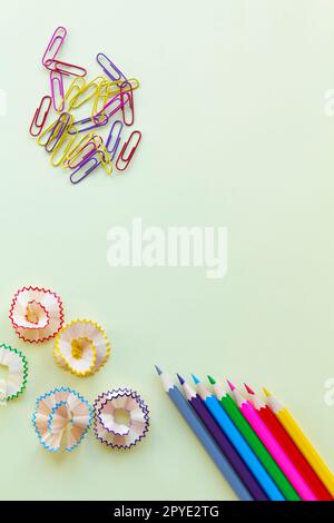 Die Buntstifte in den Ecken sind mit Spänen und farbigen Büroklammern auf hellgelbem Hintergrund für Büro- und Schularbeiten geschärft. Stockfoto