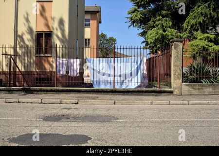 Wäscheleine in einem Hof einer Eigentumswohnung, die im Frühling von einem Zaun am Straßenrand in einem Dorf in der italienischen Landschaft gesehen wurde Stockfoto