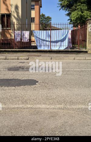 Wäscheleine in einem Hof einer Eigentumswohnung, die im Frühling von einem Zaun am Straßenrand in einem Dorf in der italienischen Landschaft gesehen wurde Stockfoto