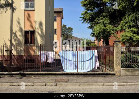 Wäscheleine in einem Hof einer Eigentumswohnung, die im Frühling von einem Zaun am Straßenrand in einem Dorf in der italienischen Landschaft gesehen wurde Stockfoto