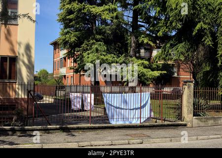 Wäscheleine in einem Hof einer Eigentumswohnung, die im Frühling von einem Zaun am Straßenrand in einem Dorf in der italienischen Landschaft gesehen wurde Stockfoto