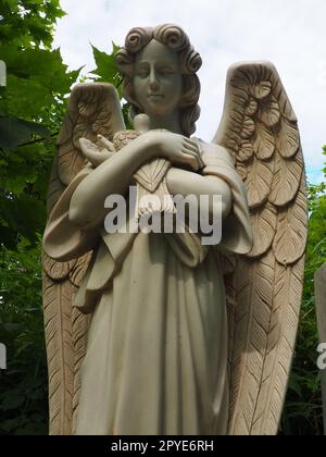 Ein Engel mit einer Taube. Skulptur auf dem Friedhof. Die Gestalt eines Engels mit Flügeln, der einen Vogel in den Armen hält. Klagen für den Verstorbenen. Grabstein-Denkmal auf einem christlichen Grab. Traurigkeit und Trauer Stockfoto