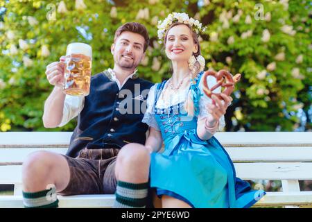 Ein Paar in Bayern sitzt auf der Bank und toasten mit Bier Stockfoto