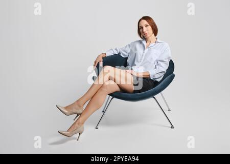 Elegante Seniorin in Minirock und weiß sitzt im Sessel Stockfoto