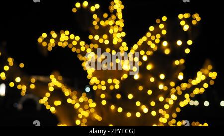 Bokeh am Weihnachtsabend. Wunderschöne runde Bokeh-Highlights. Goldene und gelbe Farben blinken im Dunkeln. Festlicher Hintergrund für Neujahr Frohe Weihnachten. Verschwommene Unschärfe-Effekte. Dekoration der Straßen der Stadt. Stockfoto