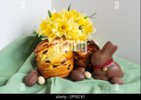 Hausgemachtes traditionelles Ostergebäck liegt auf einer grünen Serviette zusammen mit Narzissen, Kaninchen und Schokoladeneiern. Osterbacken und Dekoration. Stockfoto