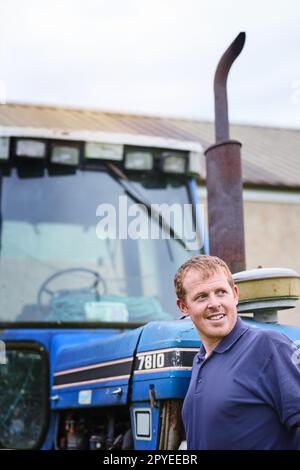 Auf die Besten in der Agrarindustrie ausgerichtet. Ein Landwirt, der neben einem Traktor auf einem Hof steht. Stockfoto