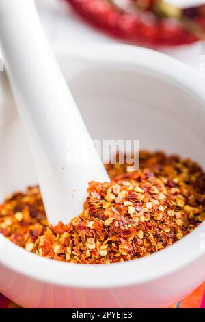 Trockene Chili-Pfefferflocken. Zerkleinerte rote Paprika in Mörtel auf weißem Tisch. Stockfoto