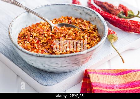 Trockene Chili-Pfefferflocken. Zerkleinerte rote Paprika in der Schüssel auf dem weißen Tisch. Stockfoto