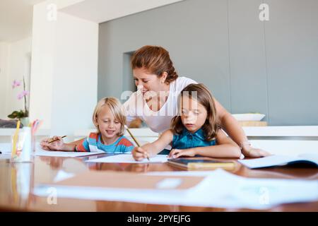 Machen Sie Ihr Zuhause zu einem angenehmen Lernumfeld. Eine junge Mutter, die ihren beiden kleinen Kindern bei ihren Hausaufgaben zu Hause hilft. Stockfoto