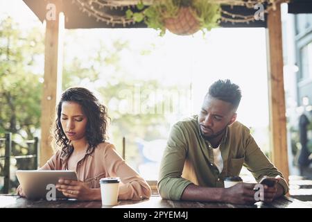 Ich Frage mich, mit wem sie redet. Zwei junge Menschen, die ihre Wireless-Geräte in einem Café verwenden. Stockfoto