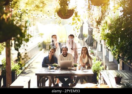 Es ist kein typisches Meeting. Freigestelltes Porträt eines Teams von Kollegen, die während eines Meetings in einem Café im Freien gemeinsam einen Laptop verwenden. Stockfoto