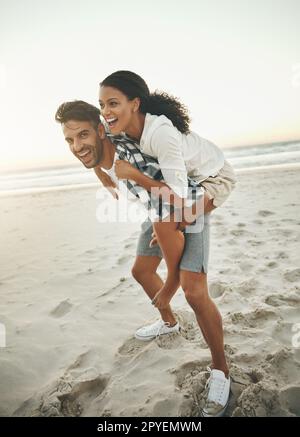 Liebe macht die Welt zum Laufen. Ein junger Mann, der seine Freundin mit dem Huckepack verbringt, während er den Tag am Strand verbringt. Stockfoto