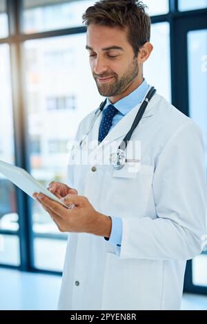 Jetzt hat er alle Patientenakten an einem Ort. Ein beschäftigter Arzt, der die Krankenakte eines Patienten auf seinem Tablet überprüft. Stockfoto