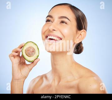 Frau, Gesicht oder Hautpflege leuchten mit Avocado auf blauem Hintergrund in Studio Healthcare Wellness, Pflege Routine oder Bio-Lebensmittel Dermatologie. Lächeln, Happy oder Beauty Model mit diätetischen Früchten für eine entspannte Gesichtsbehandlung Stockfoto