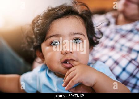 Sehr neugierig zu sein. Porträt eines fröhlichen kleinen Jungen, der tagsüber auf dem Schoß seines Vaters sitzt und in die Kamera schaut. Stockfoto