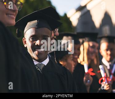 Diese Jahre waren es wert. Porträt eines lächelnden Universitätsschülers am Abschlusstag mit Mitschülern im Hintergrund. Stockfoto