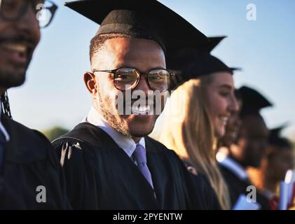 Du holst raus, was du reingetan hast. Porträt eines lächelnden Universitätsschülers am Abschlusstag mit Mitschülern im Hintergrund. Stockfoto