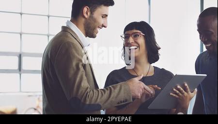 Du hast das alles allein gemacht. Eine Gruppe junger Designer, die sich ein digitales Tablet in ihrem Büro ansehen. Stockfoto