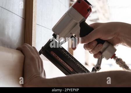 Nahaufnahme nicht erkennbare männliche Hände benutzen pneumatischen Nagler, Tacker Pistole für Holzplanke draußen. Haus bauen, Zimmermann Stockfoto