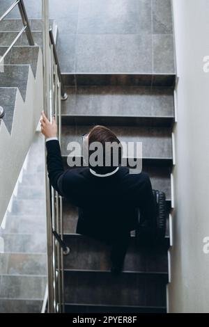 Ein Geschäftsmann mit einem Koffer läuft die Treppe im Hotel hinauf. Draufsicht. Stockfoto