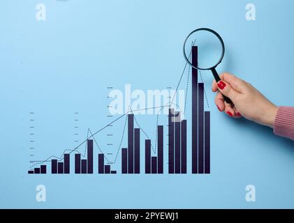 Die Hand einer Frau hält eine Lupe und ein Diagramm mit wachsenden Indikatoren, studieren Daten, analysieren Statistiken Stockfoto