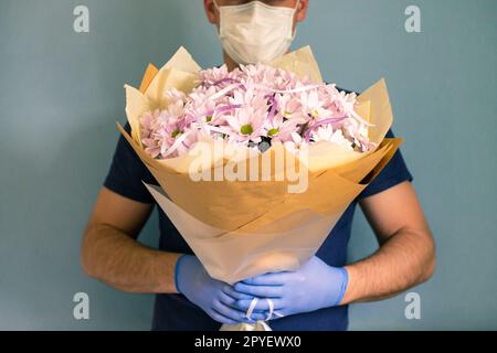 Kurier in medizinischen Handschuhen und Maske liefert Chrysanthemen. Kontaktlose Blumenlieferung. Quarantäne. Coronavirus. Stockfoto