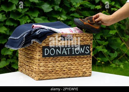 Hand, die ein Kinderschuhe in eine Box für Spenden auf einem grünen Hintergrund. Wohltätigkeitskonzept und Spendenkonzept. Speicherplatz kopieren. Stockfoto