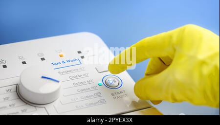 Finger in gelbem Handschuh, der kurz davor ist, den Schalter an der Atomwaschmaschine zu drücken Stockfoto