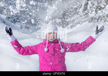 Junge Frau in Rosa ski Jacke, Handschuhe und Winter hat, lächelnd, Schnee werfen in die Luft Stockfoto