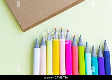 Viele bunte Filzstifte zum Zeichnen in einem Notizbuch und Album auf gelbem Hintergrund. Stockfoto