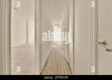 Ein langer Flur mit weißen Wänden und Holzfußboden auf jeder Seite, der zu den anderen Zimmern führt Stockfoto