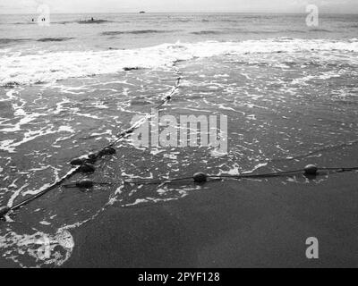 Bojen an einem Seil in der Nähe von Meerwasser. Die Rettungsringe fixieren die Menschen, um sie auf die Wassertiefe aufmerksam zu machen. Abgrenzung eines Ortes an einem Sandstrand zwischen Hotels. Winken Sie mit Seifenblasen. Schwarzweißfoto monochrom Stockfoto