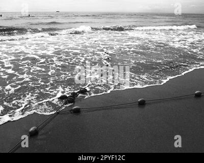 Bojen an einem Seil in der Nähe von Meerwasser. Die Rettungsringe fixieren die Menschen, um sie auf die Wassertiefe aufmerksam zu machen. Abgrenzung eines Ortes an einem Sandstrand zwischen Hotels. Winken Sie mit Seifenblasen. Schwarzweißfoto monochrom Stockfoto