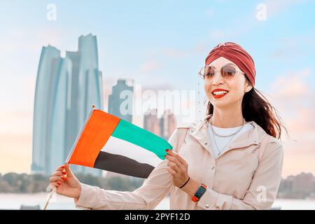 Indisches Mädchen mit VAE-Flagge vor malerischen Wolkenkratzern in Abu Dhabi. Einwanderung, Studentenausbildung und Staatsbürgerschaftskonzept der arabischen emirate Stockfoto