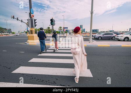 15. Januar 2023, Abu Dhabi, Vereinigte Arabische Emirate: Roller und Mädchen überqueren die Straße an der Zebraüberquerung. Regeln und Fußgängersicherheit auf den Straßen der Stadt Stockfoto