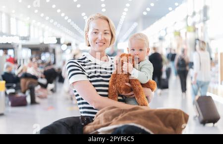 Mutter reist mit Kind, hält sein Baby am Flughafen-Terminal und wartet darauf, an Bord eines Flugzeugs zu gehen. Das Konzept „Reisen mit Kindern“. Stockfoto