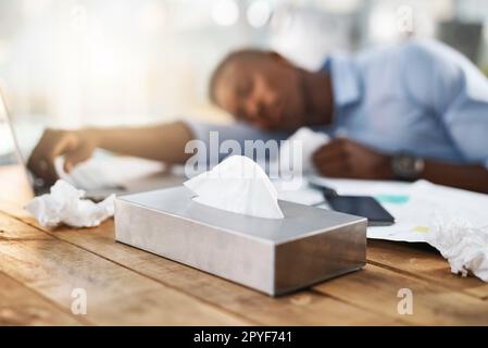 Er hat heute einen gefürchteten Arbeitstag. Ein junger Geschäftsmann, der erkältet ist, während er an seinem Schreibtisch sitzt. Stockfoto