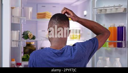 Rückansicht Eines verwirrten jungen Mannes, der Essen anschaut Stockfoto