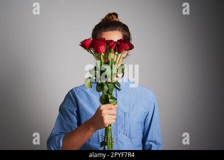 Blumen der Liebe. Studiofoto eines unbekannten Mannes, der Blumen vor grauem Hintergrund hält. Stockfoto